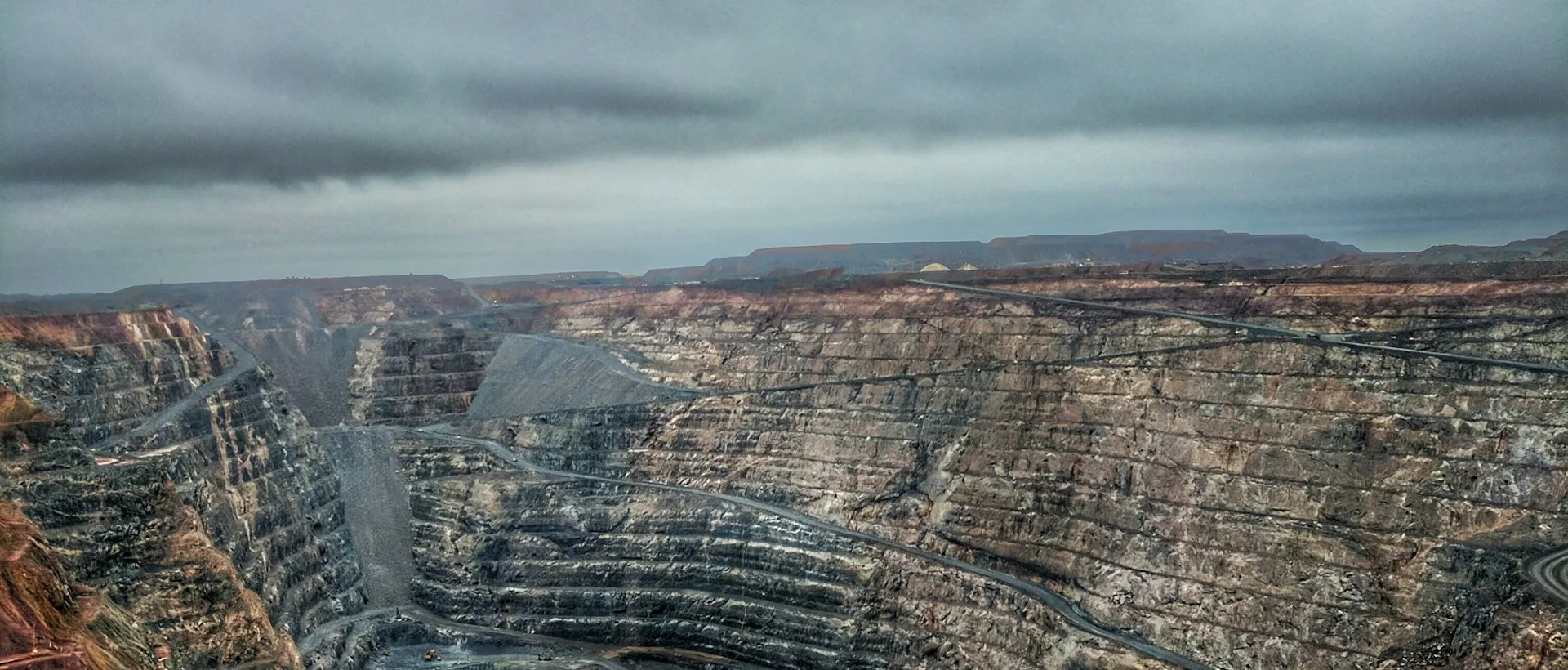 A terraced open pit mine under a heavy sky